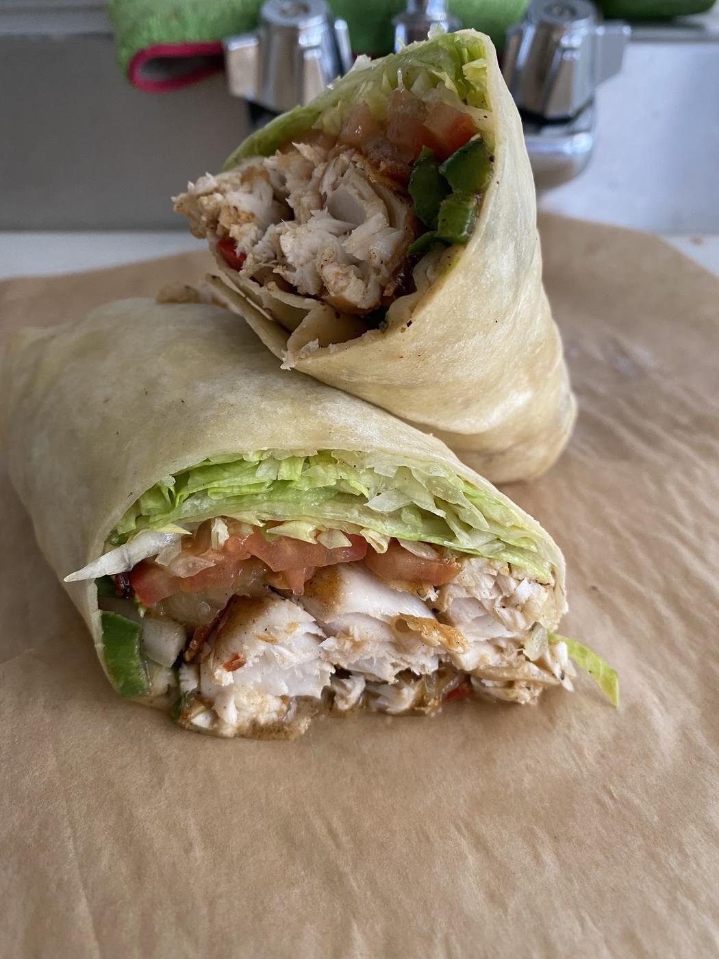 Two halves of a chicken wrap stacked on parchment paper