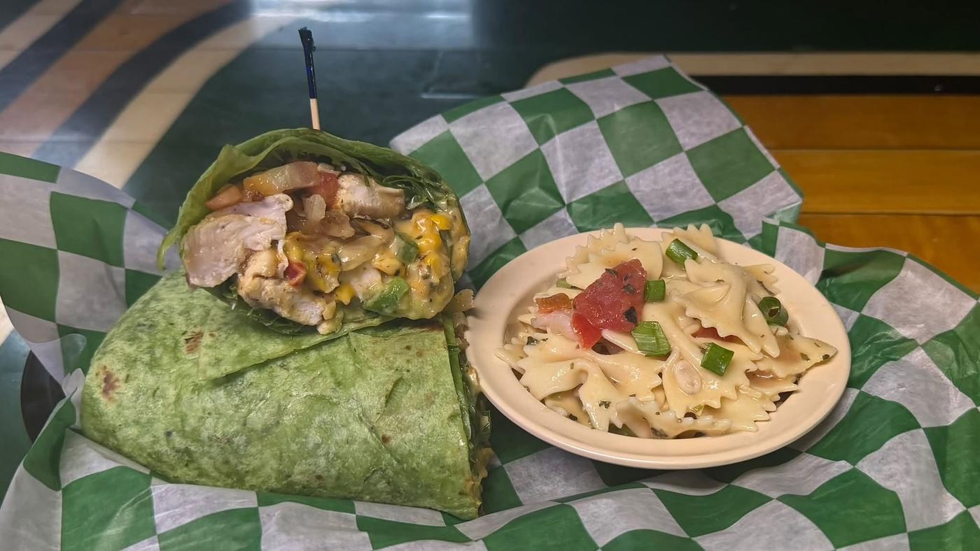A grilled chicken wrap in a spinach tortilla, cut in half, with a plate of pasta salad