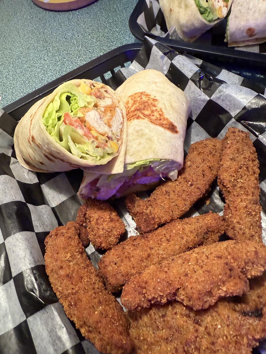 A wrap cut into halves beside a basket of breaded chicken strips
